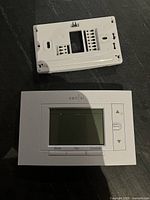 Front view of white Emerson Sensi ST55 smart thermostat with screen and control buttons alongside the white wall plate showing terminal connections.