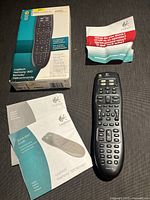 Logitech Harmony 300 remote with box, manual, and pamphlet laid out on surface.