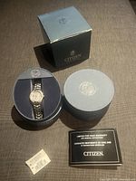 Citizen Eco-Drive wristwatch in original round display box with warranty card, tag, and packaging box visible.