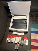 Canon TS8320 printer open showing scanner bed and multiple new ink cartridges below it, some in boxes and some loose.