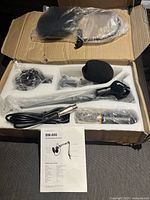 Open box with all components of the microphone bundle including mic, shock mount, pop filter, arm stand with clamp, cables, and instruction manual.