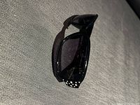 Angie VL black sunglasses folded with rhinestone detail visible on the temple arms, shown on gray fabric surface.