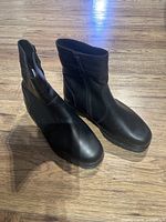 Front top view of pair of black leather men's boots with side zippers, placed on wooden floor.