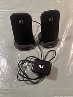 Two black IQ wireless chargers upright with IQ branded adapter cable in front on a silver surface.