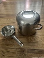 Top view of two stainless steel pots, one smaller with glass lid and long handle, and one larger with stainless steel lid and loop handles.