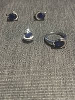 Silver earring, ring and brooch set with blue oval stones displayed on fabric surface.