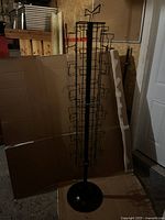 Full view of the black metal wire card rack standing against cardboard and other background items, showing height and structure.