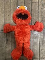 Full view of red Tickle Me Elmo plush toy lying on wooden floor with arms and legs spread out