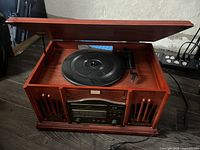 Top open view showing the record player platter and tonearm inside a wooden lid-top cabinet with built-in speakers and radio controls below.
