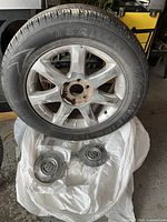 Single tire mounted on a chrome Buick rim with two Buick center caps placed below on a white sheet. Tire and rim show dirt and signs of use.