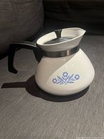 Front side view of the white ceramic tea kettle with blue floral pattern and black handle and lid.
