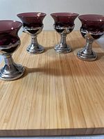 Four purple glass liquor glasses with silver metal stems and bases arranged on a wooden surface.