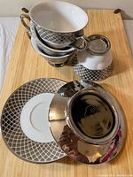Stack of 4 porcelain teacups with metallic lattice pattern and four matching saucers showing design and pattern