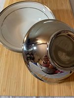 4 white porcelain soup bowls with silver or platinum rim, displayed on wood surface. One bowl is flipped showing shiny base and a slight reflection.