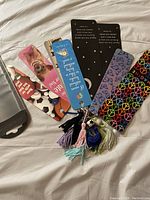 Top view showing all 8 bookmarks fanned out on a white background, each with a colorful design and tassels attached.