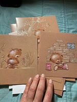 Set of bear-themed cards showing three teddy bear designs on the front. Brown tones with pastel details of bears holding or sitting by objects.