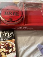 Packaged lot with red labeled brie baking dish lid and red toppings box in original packaging, with small recipe or information card included.