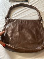 Front view of the brown leather handbag showing padded shoulder strap and overall leather texture.
