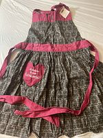 Full view of Kitchen Diva apron showing halter neck and waist ties, maroon and black patterned fabric, heart-shaped pocket embroidered 'Kitchen Diva'.