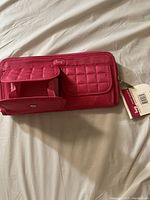 Pink Lug double backflip wallet lying on a white fabric surface showing front flap coin pouch with snap closure and attached tag.