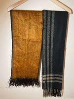 Two scarves hanging on a hanger, one brown and one black plaid, showing overall colors and fringed ends.