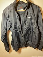 Front view of black Nike jacket with zipper, elastic cuffs, and white swoosh logo on chest.