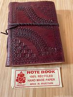 Closed handmade leather notebook showing embossed leaf and geometric patterns on the cover and a leather tie closure.