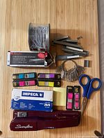 Photo showing the heavy duty Swingline stapler, boxes of staples, large paper clips, metal key rings, colorful sticky page markers, scissors, and sticky notes on wooden surface.