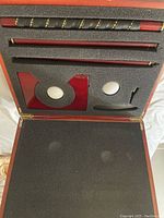 Top view of the mini golf set inside the wooden case showing foam inserts holding three putter sections, two golf balls, the golf hole with flag, and the putter head.