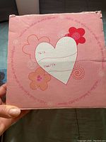 Palm holding pink box top showing heart and flower designs with 'To/À' and 'From/De' fields.