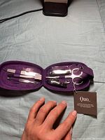 Opened purple velvet manicure case showing various nail tools held in elastic bands including scissors and clippers.