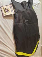 Top view of black dog storm coat with yellow trim and 'RC Pets' logo on back. Tag attached showing product information.