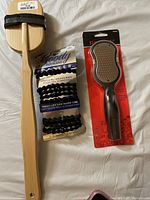 Long wooden bath brush, Goody touchless hair bands, and Revlon callus remover in packaging shown on white surface.