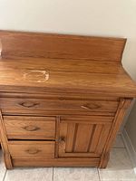 Front view of the antique wood washstand showing three drawers and cabinet door with wood handles.
