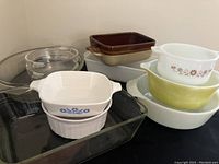 General assortment of vintage Pyrex glass and ceramic baking dishes showing various shapes, sizes and colors including clear glass, brown and tan ceramic pans, white and colored ceramic dishes and bowls.