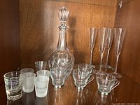 Wide view of all items including decanter, champagne flutes, espresso cups, and shot glasses on wooden shelf