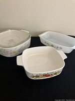 Set of three vintage casserole dishes: round CorningWare with lid, square CorningWare, rectangular Pyrex with floral pattern.