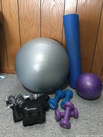 View showing all items: silver exercise ball, blue yoga mat, purple small exercise ball, blue and purple dumbbells, black ankle weights