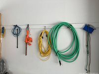 Items hung on wall including green garden hose, yellow extension cords, Black and Decker orange hedge trimmer, and bungee cords in black and blue.