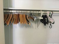 Photo showing a variety of wooden, pant, and plastic hangers on a metal rod attached to a wall bracket.