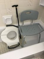 Photo showing the adjustable bath chair, toilet seat adapter, and adjustable cane placed inside a bathtub with textured matting.