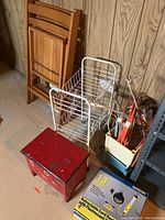 Photo of folding chairs, white wire shoe rack, red wooden shoe shine step stool, extension cords, and retractable cord reel on basement floor.