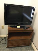 Photo of Insignia 19-inch TV and brown laminate pivoting top stand with remote on top.
