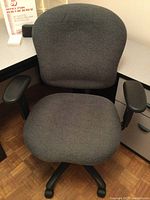 Gray fabric upholstered adjustable office chair with armrests and five caster wheels shown from front view.