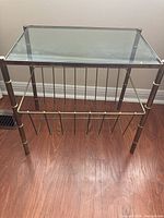 Front and top view of the magazine rack showing clear glass top and bronze metal frame with gold ring accents.