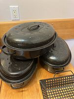 Three black granite ware roasting pans with lids stacked on counter.