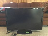 Full frontal view of the Sharp Aquos 36-inch TV on stand with two remote controls placed in front.