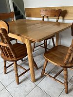 Photo showing the rectangular solid wood table with drop leaf extended and four matching chairs around it on tiled floor.