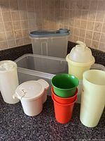Vintage Tupperware assortment including food storage containers, cups, and drink jug arranged on a kitchen countertop.