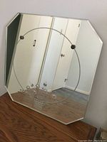 Full view of the octagonal vintage mirror standing on a wooden surface, showing the etched floral basket design centrally placed within a large circular etched frame on the glass.